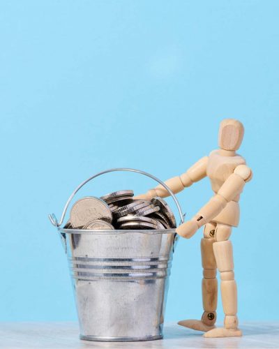 A wooden mannequin and coins in a miniature bucket on a blue background, a concept of high income, subsidy